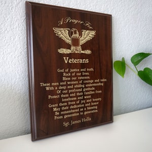 Puede incluir: Una placa de madera con una inscripci&oacute;n dorada que dice "Una oraci&oacute;n por los veteranos". La placa presenta un emblema de &aacute;guila dorada y un poema en honor a los veteranos.