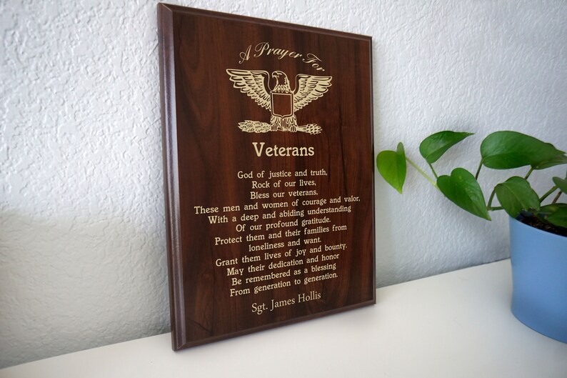 Puede incluir: Una placa de madera con una inscripci&oacute;n dorada que dice "Una oraci&oacute;n por los veteranos". La placa presenta un emblema de &aacute;guila dorada y un poema en honor a los veteranos.