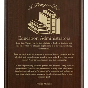 May include: A brown wooden plaque with gold lettering that reads "A Prayer For Education Administrators". The plaque features a stack of books and a prayer for education administrators.
