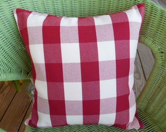 May include: Red and white gingham pillow with a square pattern. The pillow is sitting on a green wicker chair.