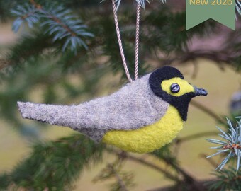 May include: A felt bird ornament featuring a gray back, a bright yellow belly, and a black head with a small dark eye. The bird has a pointed beak and hangs from a thin, twisted cord. A green tag in the upper corner displays the text New 2026.