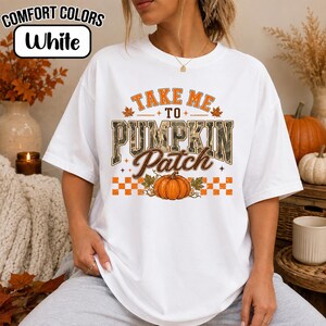 May include: A white short-sleeve t-shirt featuring the orange and brown text Take Me To Pumpkin Patch. The design includes a central orange pumpkin graphic, autumn leaf accents, and a checkered pattern border on a Comfort Colors brand shirt.