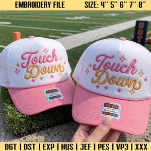 Op de afbeelding: Twee witte en roze truckerpetten met de geborduurde tekst Touch Down in roze en goudkleurig schrift, versierd met kleine sterretjes. Elke pet heeft een sticker op de klep met de tekst OTTO CLASSIC TOUCH DOWN EDITION 001.