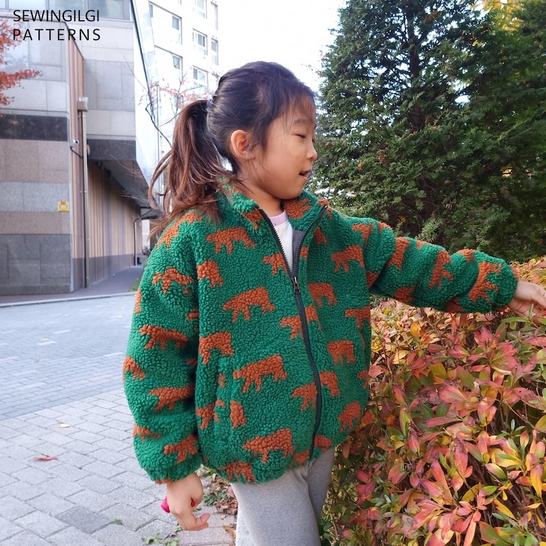 May include: A green fleece jacket with a repeating pattern of brown bear silhouettes, featuring a high collar, a full-length black front zip, and long sleeves. The text SEWINGILGI PATTERNS is visible in the upper left corner.
