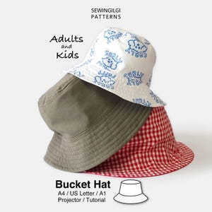 May include: Three bucket hats stacked together. The top hat is white with a blue repeating pattern of a curly-haired dog and the text 'CURLY PUPPY'. The middle hat is solid olive green. The bottom hat features a red and white gingham pattern.
