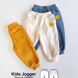 Può includere: Tre paia di pantaloni jogger per bambini in giallo senape, crema e blu, con vita e polsini elastici. I jogger color crema e blu presentano una toppa gialla a forma di cuore con una faccina sorridente. Testo: SEWINGILGI PATTERNS e Kids Jogger Sewing Pattern.