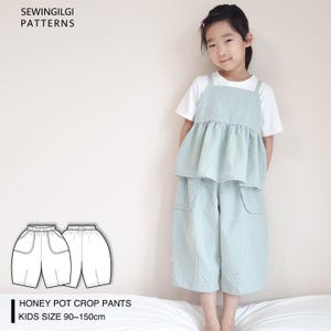 Op de afbeelding: Een naaipatroon voor Honey Pot Crop Pants voor kinderen, maten 90-150 cm. Het patroon bevat twee illustraties van de broek, een vooraanzicht en een achteraanzicht. De broek heeft een wijde pijp en twee grote zakken aan de voorkant.