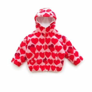 May include: A hooded jacket made of pink and red heart-patterned fleece material with a front zip closure. The text SEWINGILGI PATTERNS is visible in the upper left corner. The jacket features long sleeves and a white interior lining.