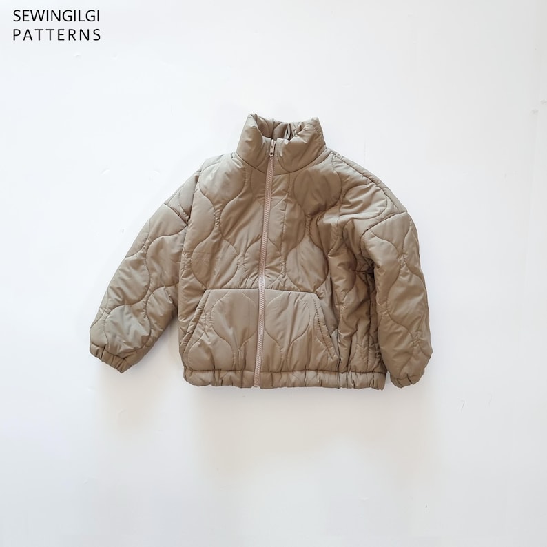 May include: A beige quilted jacket with a high collar, a full-length front zip, and long sleeves with elasticated cuffs. The jacket features a repeating curved pattern across the fabric and includes the text SEWINGILGI PATTERNS.