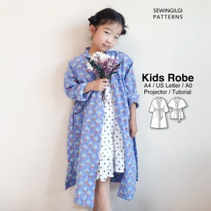 Op de afbeelding: Een blauwe kamerjas met een herhalend patroon van lichtblauwe en rode bloemvormen. De tekst luidt SEWINGILGI PATTERNS, Kids Robe, A4 / US Letter / A0, Projector / Tutorial, met twee lijntekeningen van kamerjassen met verschillende mouwlengtes.