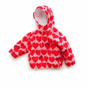 May include: A hooded jacket made of fuzzy, textured material featuring a repeating pattern of red hearts on a light pink background. The jacket has a front zip closure and a white interior lining. The text SEWINGILGI PATTERNS is visible.