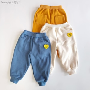 Peut inclure: Trois paires de pantalons de survêtement avec un patch en forme de cœur souriant. Une paire est bleue, une est blanche et une est jaune.
