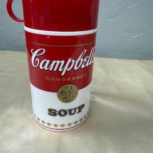 May include: A red and white Campbell's Soup travel mug with a handle. The mug features the Campbell's Condensed Soup logo in white on a red background. The word "SOUP" is printed in gold.