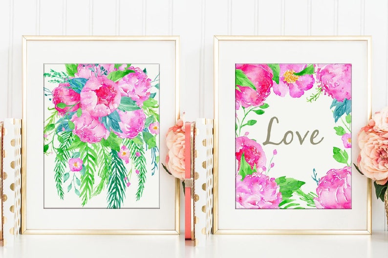 May include: Two framed watercolor prints with pink flowers and green leaves. The print on the left features a bouquet of pink peonies. The print on the right features a wreath of pink peonies with the word "Love" in the center.