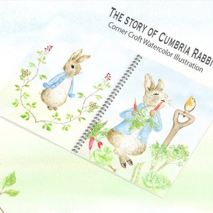 May include: An open book with a watercolor illustration of a rabbit in a blue jacket. The book's title is "The Story of Cumbria Rabbit" with the subtitle "Corner Croft Watercolor Illustration".