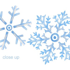 Puede incluir: Dos copos de nieve azules de acuarela con centros blancos. Los copos de nieve est&aacute;n sobre un fondo blanco. El texto "close up" est&aacute; escrito debajo de los copos de nieve.