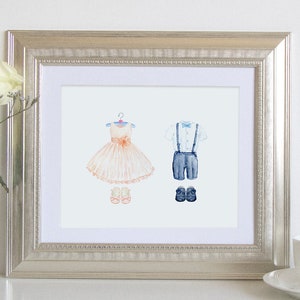 May include: A framed watercolor illustration of a girl's dress and a boy's outfit. The girl's dress is peach and white with a pink bow. The boy's outfit is blue and white with a bow tie. Both outfits are hanging on hangers.