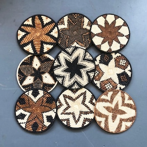 May include: Nine round woven wall decor pieces in black, white, and brown. The pieces have a variety of geometric patterns.