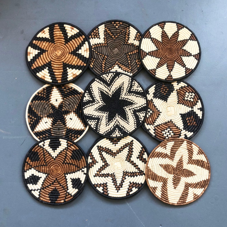 May include: Nine round woven wall decor pieces in black, white, and brown. The pieces have a variety of geometric patterns.