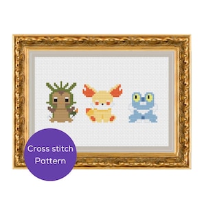 May include: Cross-stitch pattern featuring three colorful cartoon creatures. The framed artwork includes a green, brown, and tan creature, a yellow and orange fox-like character, and a blue frog-like figure. The frame is gold and the background is white.