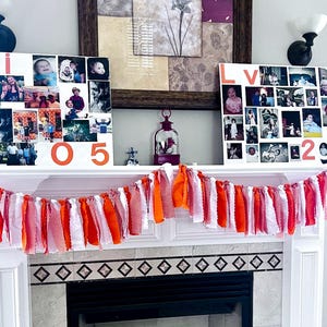 May include: A white mantelpiece decorated with a garland of orange, red, and white fabric strips. Above the mantel are two white canvases with photos and the numbers "05" and "2022" in orange. The canvas on the left has the name "Kni" in red.