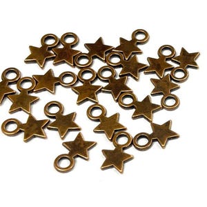 May include: A group of 18 antique gold-toned metal star charms with jump rings. The charms are scattered on a white background.