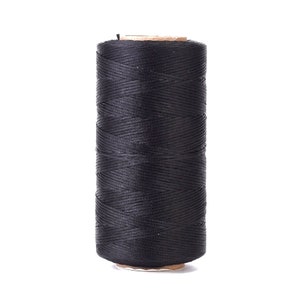 May include: A spool of black thread, tightly wound and cylindrical in shape. The thread is a solid, dark color, and the spool has a cardboard base and top. The thread appears to be new and unused.