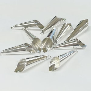 May include: A group of silver metal cones with a pointed tip and a flared opening. The cones are arranged in a random pattern on a white surface.