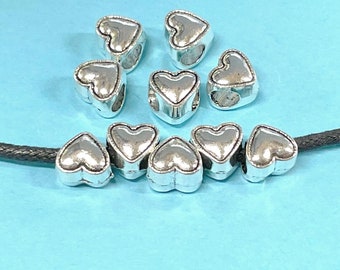 May include: A set of silver heart-shaped beads with a hole in the center. The beads are strung on a black cord.