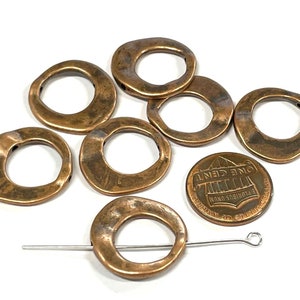 May include: Seven copper-colored metal rings with an irregular, hammered finish. The rings are approximately the size of a US penny.