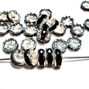 May include: A group of silver-toned metal bead caps with black rhinestone accents. The bead caps are arranged in a loose pile with a few strung on a silver wire.