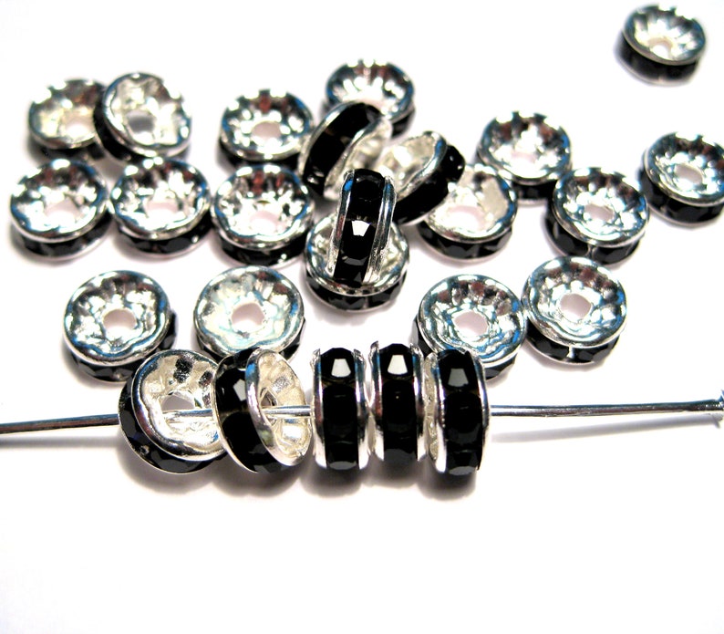 May include: A group of silver-toned metal bead caps with black rhinestone accents. The bead caps are arranged in a loose pile with a few strung on a silver wire.