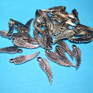 May include: A pile of silver angel wing charms, perfect for jewelry making or crafting projects.