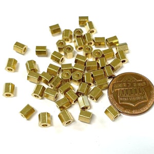 May include: A pile of gold-colored metal spacers, some are hexagonal in shape, and some are round. The spacers are scattered on a white surface next to a US penny.