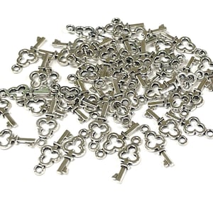 May include: A large pile of silver-toned metal key charms with a clover-shaped design. The keys are scattered on a white background.
