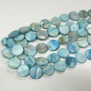 May include: Strands of round, flat, blue-green shell beads. The beads have a pearlescent sheen and vary in shades of blue and green. The beads are strung together, ready for jewelry making or other crafts.