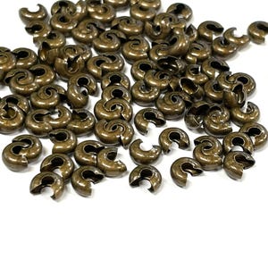 May include: A large pile of antique gold-toned metal crimp beads. The beads are shaped like a half-circle with a small opening on one side.