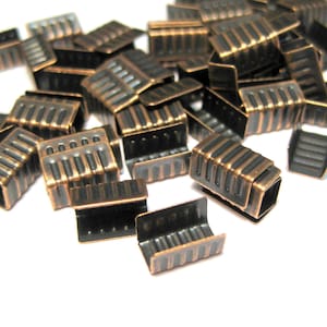 May include: A pile of antique copper-toned metal cord ends. The cord ends have a ridged design and are perfect for finishing off cords and straps.