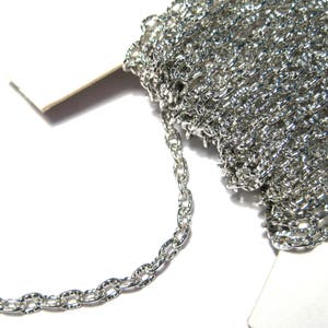 May include: A roll of silver-coloured chain, featuring a textured oval link design. The chain is partially unraveled, displaying individual links. The background is white, accentuating the chain's metallic sheen. Suitable for jewellery making or craft projects.
