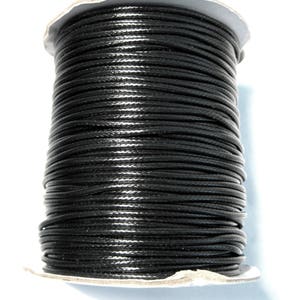 May include: A spool of black waxed cotton cord. The cord is wound tightly around the spool, creating a smooth, even surface.