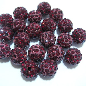 May include: A close-up of a pile of maroon-colored round beads covered in small, sparkling rhinestones.
