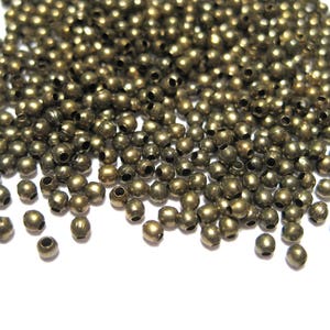 May include: A large pile of small, round, gold-colored metal beads. The beads have a hole in the center and are scattered on a white surface.