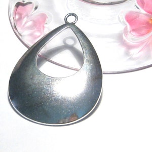 May include: A silver teardrop-shaped pendant with a large open circle in the center. The pendant has a loop at the top for attaching a chain.