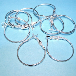 May include: A set of silver hoop earrings with a hinged clasp. The earrings are arranged in a pile on a blue background.