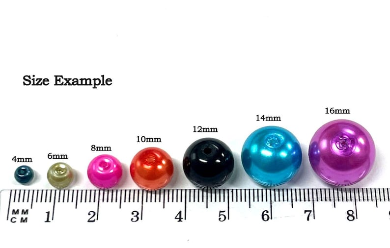May include: Size example of round plastic beads in various colors and sizes, measured on a ruler in millimeters. The beads range in size from 4mm to 16mm.