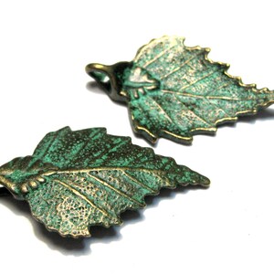 May include: Two green metal leaf charms with a textured surface. The leaves have a detailed vein pattern and a slightly aged look.