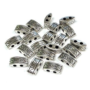 May include: Silver-colored metal beads with an oval shape and two holes. Each bead features a decorative, curved design. The beads are scattered on a white surface, suitable for jewelry making or crafting projects.