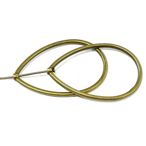 Op de afbeelding: Een paar gouden oorringen in de vorm van een traan. De oorringen zijn gemaakt van metaal en hebben een gladde afwerking.