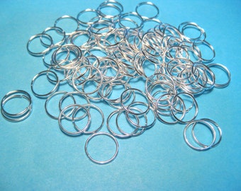 May include: A large pile of silver jump rings, a type of jewelry finding, on a blue background.