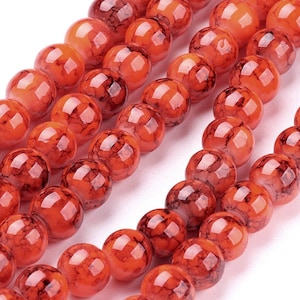 May include: Orange glass beads with black marbling. The beads are round and have a glossy finish.